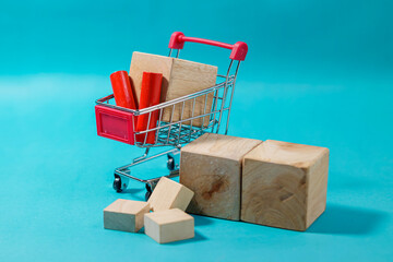 Miniature shopping cart packed with items surrounded by wooden blocks on a blue background. High Quality Photo © 7TridentSea