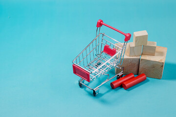 Small metal shopping cart positioned near stacked wooden blocks on a blue surface for retail, supply chain, and commerce topics. High Quality Photo © 7TridentSea