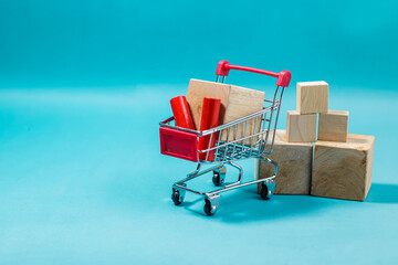 Miniature shopping cart filled with wooden blocks and items next to stacked cubes on a blue background. High Quality Photo © 7TridentSea