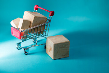 Miniature shopping cart full of wooden blocks placed next to an extra cube on a blue background for e-commerce and retail concepts. High Quality Photo © 7TridentSea
