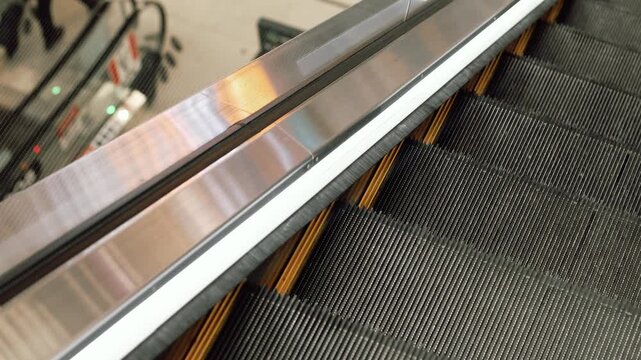 4K Slow motion video of empty moving escalator stairs. Close up top view shot of black rubber steps, metal steel handrail, and yellow safety lines in a modern shopping mall or transport terminal.