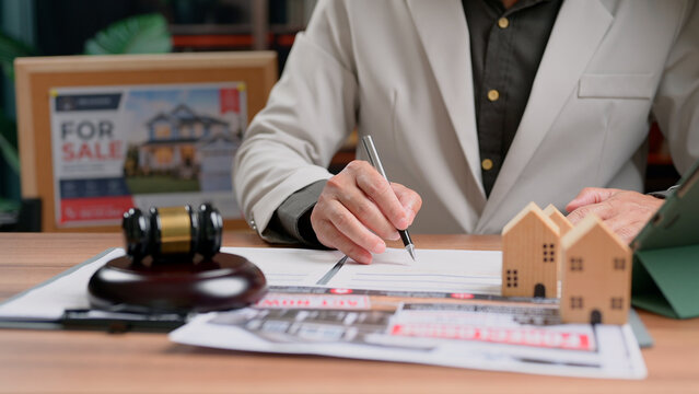 Client person signing contract document buying residential property legal agreement wood desk showing miniature house model gavel symbol business transaction process buyer reviewing terms new.