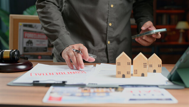 Person inspects confidential real estate contract documents wooden house models desk office legal dispute property ownership transaction auction gavel negotiator mortgage loan agreement business.