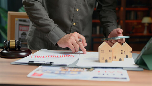 Person reviewing legal contract, wooden house model, gavel, mobile phone, office desk, real estate agreement, analyzing financial papers, commercial transaction, corporate negotiation, consultation,.