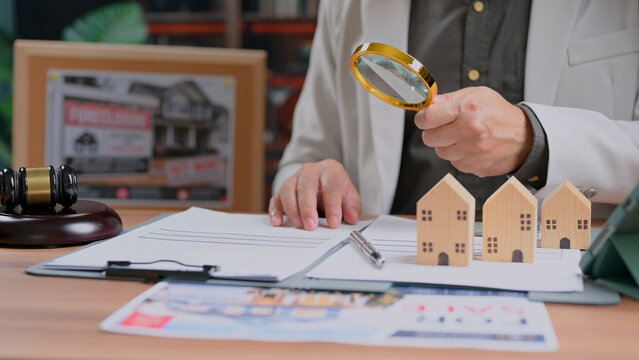 Expert inspecting miniature houses over contracts gavel real estate mortgage evaluation property purchase financial planning legal review risk assessment investment.