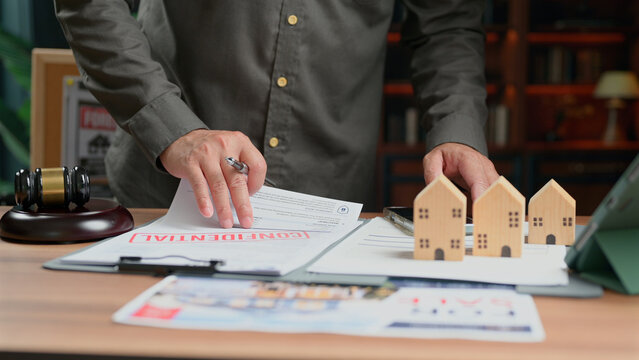 Manager signing real estate contract document near wooden house models examining property agreement legal office desk corporate transaction planning business strategy financial investment management.