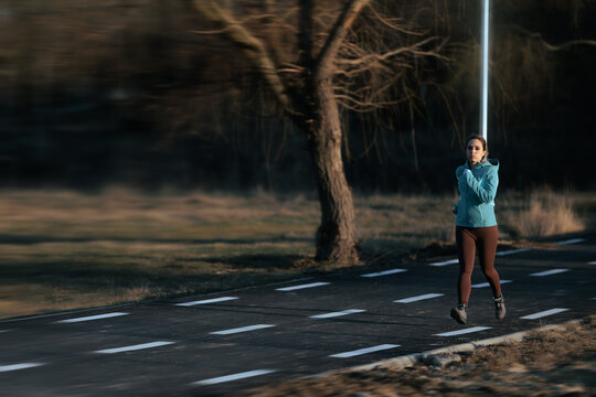 Active Female Runner Jogging On Park Trail During Autumn Workout. Determined young woman in turquoise jacket exercising outdoors on asphalt running path
