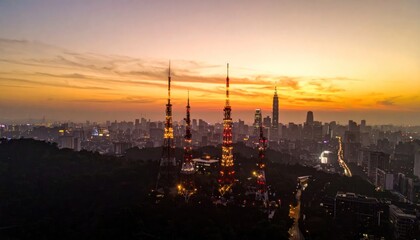 Fototapeta premium Illuminated Telecommunication Towers Stand Tall Over Taipei City Skyline at Sunset with Golden Hour Glow