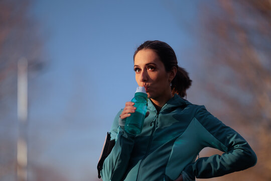 Active Female Runner Drinking Water From Shaker Bottle During Workout. Thirsty young woman in sportswear hydrating herself while exercising outdoors on sunny day