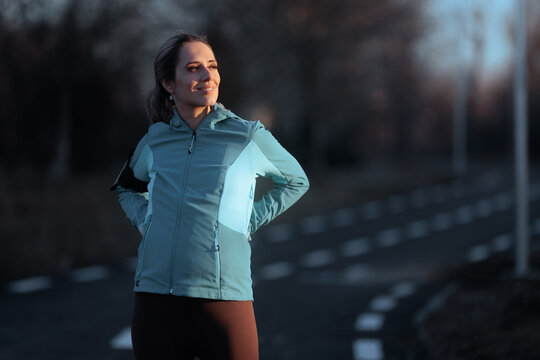 Smiling Female Runner Resting Contented After Successful Outdoor Workout. Happy young woman in sportswear standing on park path smiling thoughtfully outdoors