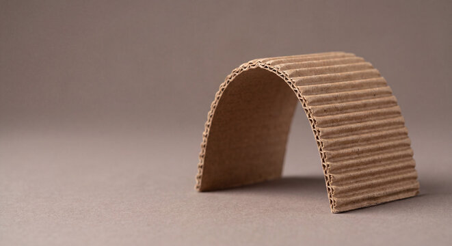 Bent corrugated cardboard arch on brown background, eco-friendly packaging material, minimal concept