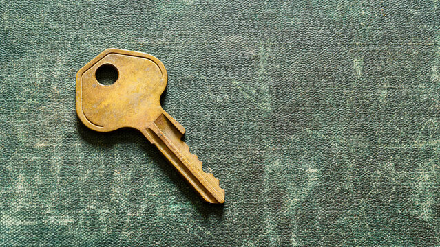 A worn metal key resting on a textured rustic green surface, representing access, security, locks, property, and home.