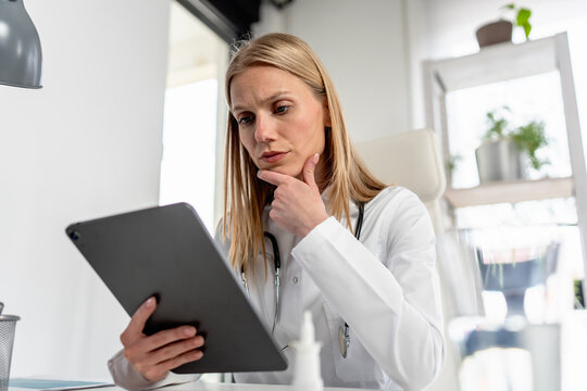 Thoughtful female physician studies information on a tablet while considering a clinical diagnosis and treatment decision