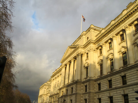 View of the Bank of England building with its neoclassical facade, columns, and a flag flying on top under a cloudy sky in London, England, United Kingdom.