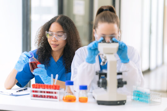 Diverse Female Scientists Conducting Research with Microscope and Chemical Flasks in Laboratory