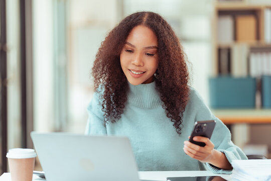 Happy Young African American Woman Using Smartphone at Desk with Laptop and Tablet