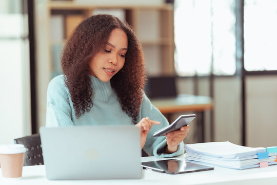 Happy Young African American Woman Using Smartphone at Desk with Laptop and Tablet