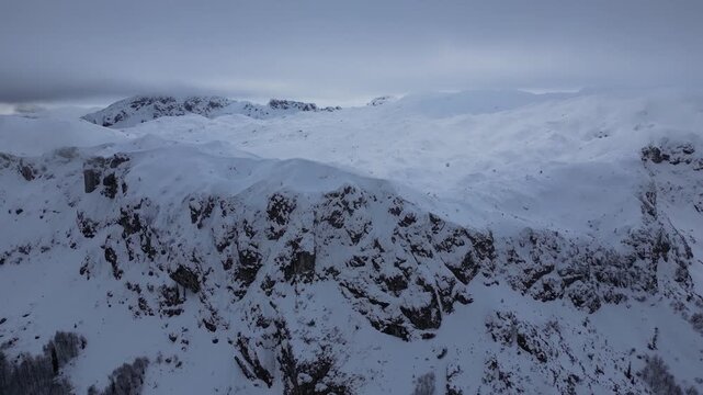 Drone View of Snow-Covered Mountain Peaks Under a Cloudy Winter Sky
