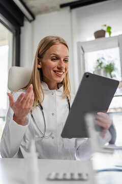 Smiling female doctor talks to a patient during a video consultation on a digital tablet in her medical office