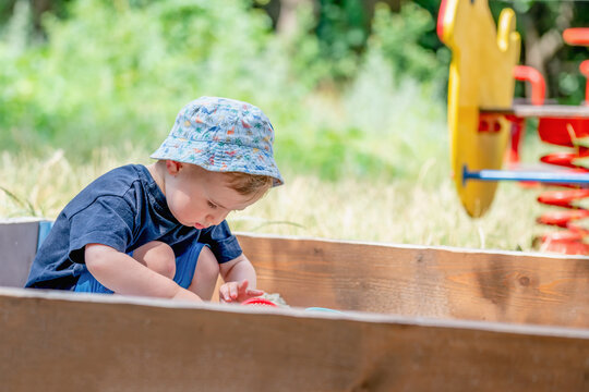 Young child crouching in a sandbox and carefully examining the sand. Copy space for text or design.