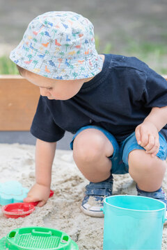 Child playing with a red toy scoop and bucket in the sand.