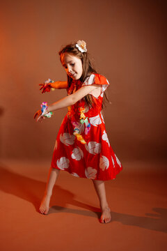 Pretty 6 years old girl in red dress with flowers is dancing in the photo studio with brown background. This photo has been taken in Prague, Czech Republic, August 2025