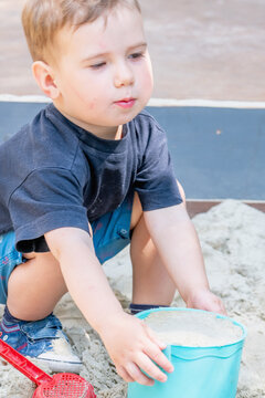 Toddler carrying a bucket full of sand while playing outdoors.