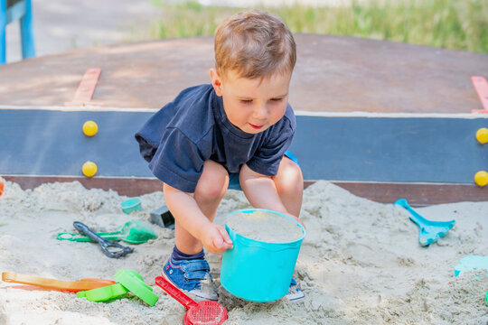 Little boy lifting a heavy bucket full of sand in a sandbox.