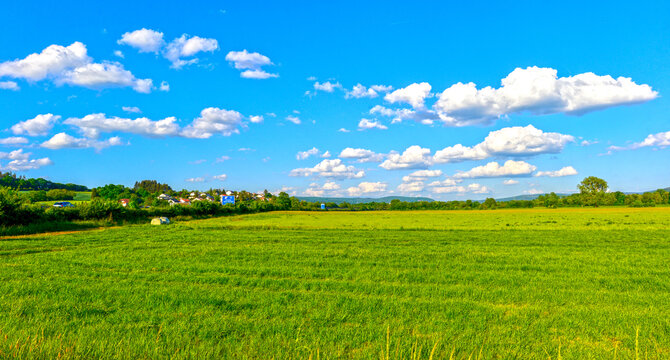 Weite gr&uuml;ne Wiesenlandschaft mit Blick auf Gr&uuml;ndau-Rothenbergen unter blauem Wolkenhimmel in Hessen