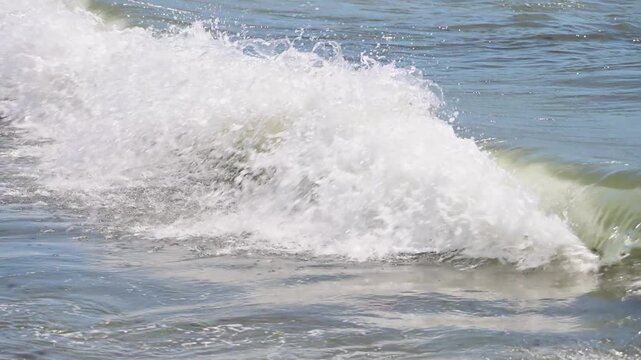 A crisp white wave crest breaks over gentle blue and green coastal water.