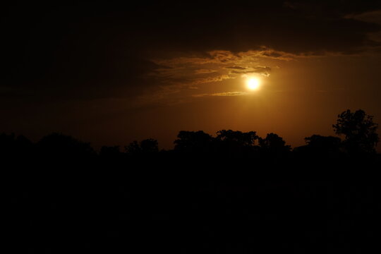 Golden sunset glowing through dramatic clouds over a dark tree line
