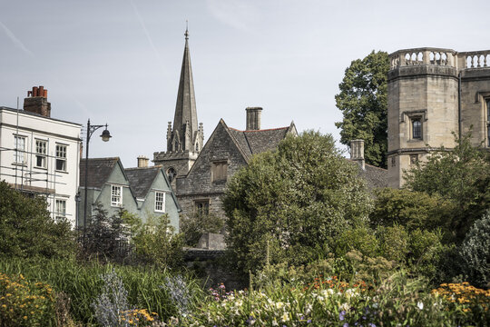 View of historic stone buildings and a church spire rising above a lush garden in Oxford, England, United Kingdom.