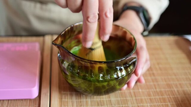 Someone using a bamboo whisk for whisking Matcha powder for drink. Whisking matcha is essential to break up clumps, create a smooth, creamy texture, and form a frothy foam on top by incorporating air.