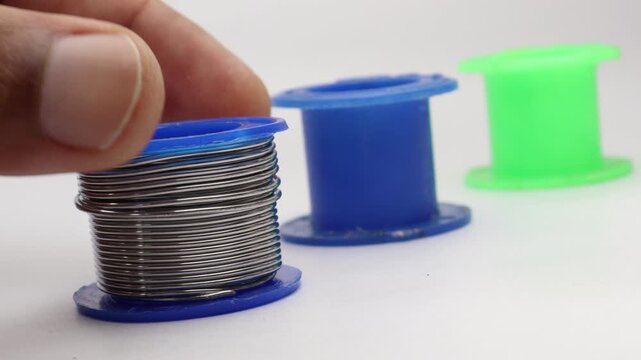 Hand turning a full spool of solder wire with several other empty spools placed beside it for comparison