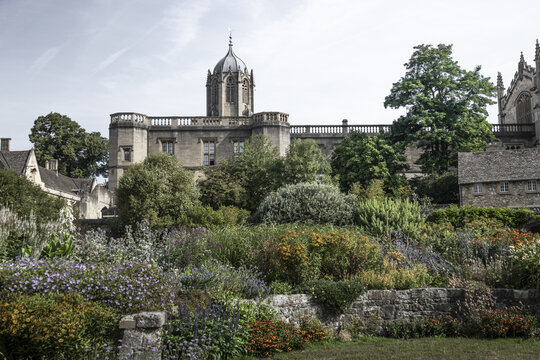 View of the historic Tom Tower at Christ Church College rising above a lush garden with stone walls and colorful flowers in Oxford, England, United Kingdom.