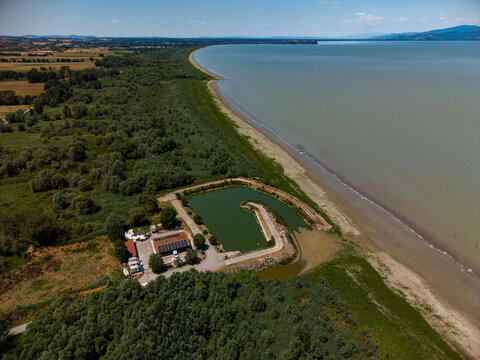Aerial view of Cooperativa fra Pescatori Stella del Lago situated on the shore of Lake Trasimeno, surrounded by lush vegetation and trees in Castiglione del Lago, Umbria, Italy.