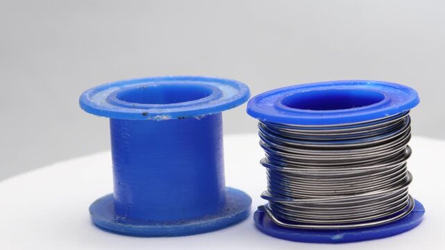 Close up of a soldering wire coil slowly turning next to an empty spool