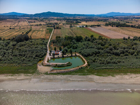 Aerial view of Cooperativa fra Pescatori Stella del Lago with its small pond, surrounding trees, and agricultural fields in Castiglione del Lago, Umbria, Italy.
