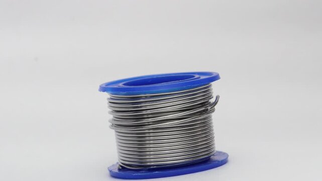 Close up of a soldering wire coil replaced with an empty spool on a white background