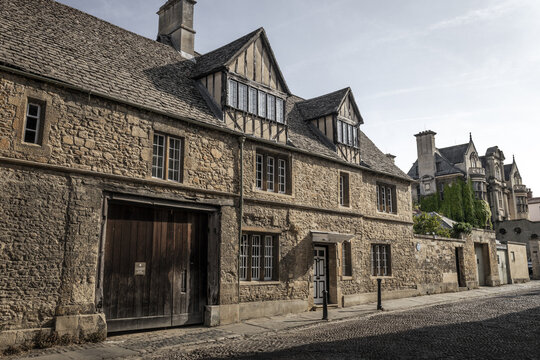 View of a historic stone building with timber-framed gables and a large wooden gate along a cobblestone street in Oxford, England, United Kingdom.
