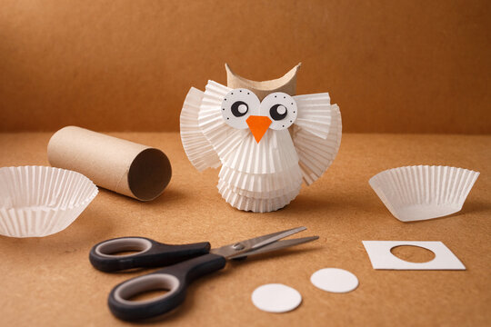 Paper owl craft made from cupcake liners and cardboard tube with scissors. Studio craft photography on kraft paper background. DIY creativity and recycling concept. soft focus