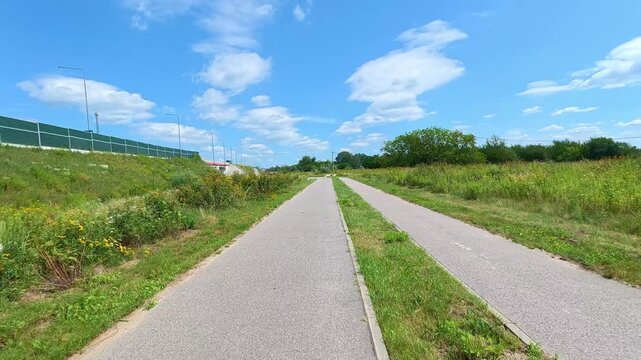 Twin paved bike path stretching through grassy verge near highway. Bicycle POV