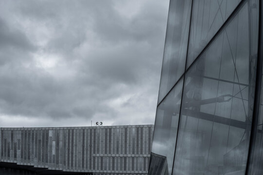 Dark clouds pass over modern architecture in Oslo, Norway, where glass and reflection stretch across an urban facade beneath the skyline.