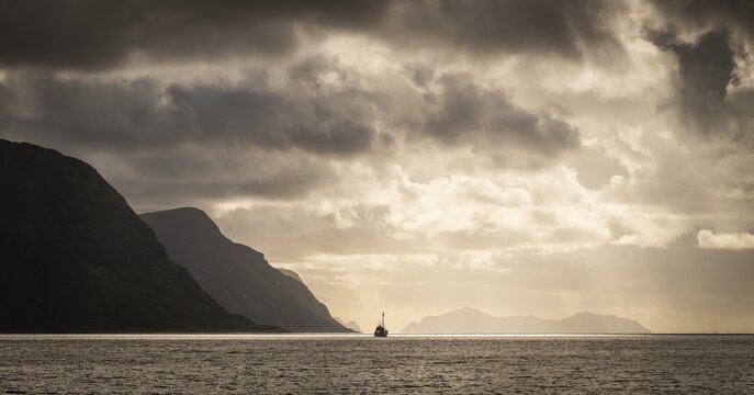 Dramatic lighting and dark clouds over the sea, island, ship, near &Aring;lesund or Alesund, M&oslash;re og Romsdal Fylke, Norway