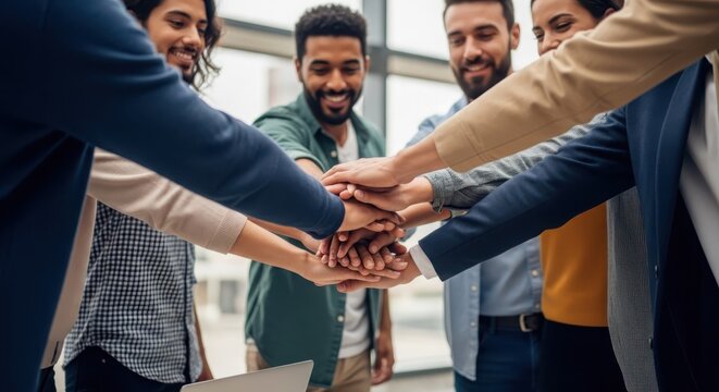 Diverse team of smiling professionals joining hands in a symbol of unity and collaboration at work