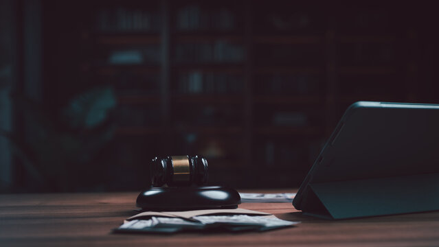 Desk displays judge gavel, cash envelope, tablet, library background depicting legal court crime corruption litigation dispute penalty negotiation verdict sentencing lawyer trial case judgment.