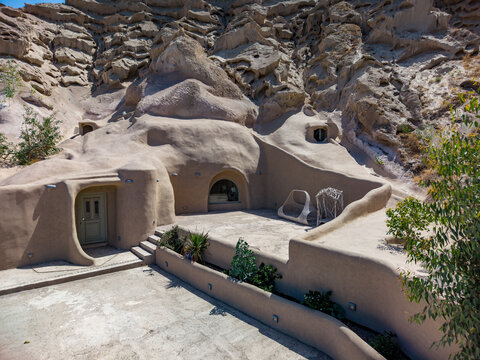 Aerial view of cave dwelling carved into volcanic rock with smooth earth-toned walls, arched doorways, and a patio area in Fira, Greece.