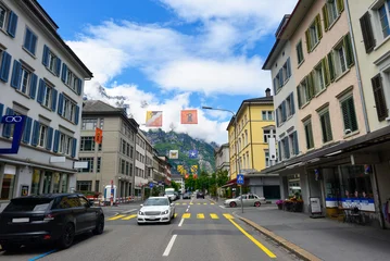 Blick entlang der Hauptstrasse in Glarus mit historischen Gebäuden und bunten Wappenbannern vor den Glarner Alpen © Ilhan Balta