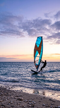 Silhouette of a windsurfer on the water at sunset, symbolizing adventure, freedom, and the power of nature