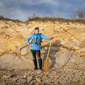 senior male paddler wearing life jacket with a wooden canoe paddle on a rocky lake shore